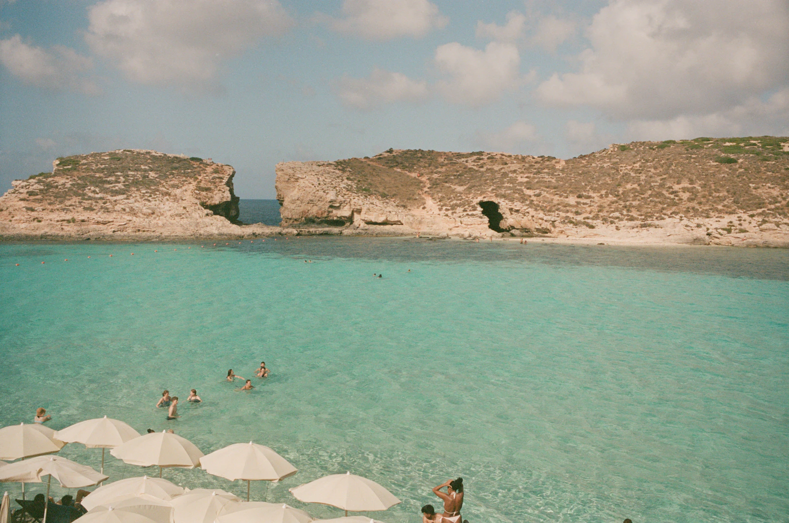 Swimmers and sun umbrellas beside the turquoise Blue Lagoon in Comino, Malta